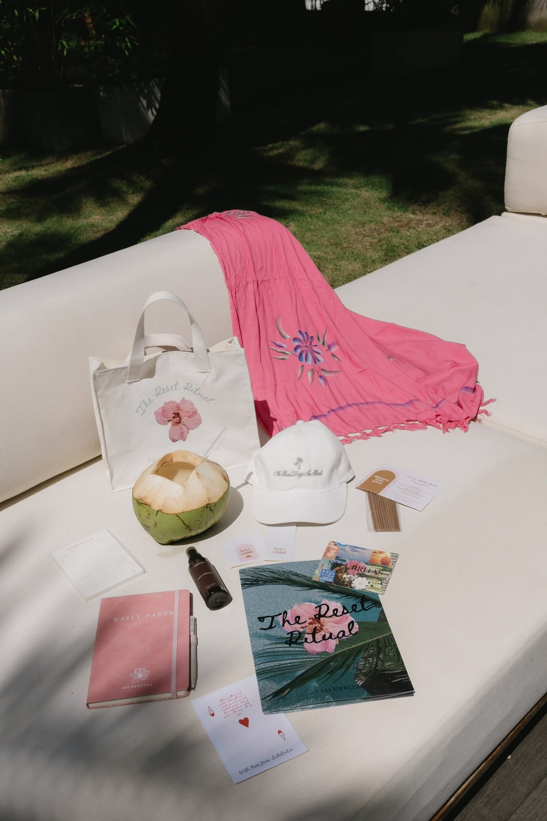 Retreat journals, a tote bag, coconut and wellness gifts arranged on a cushioned outdoor sofa